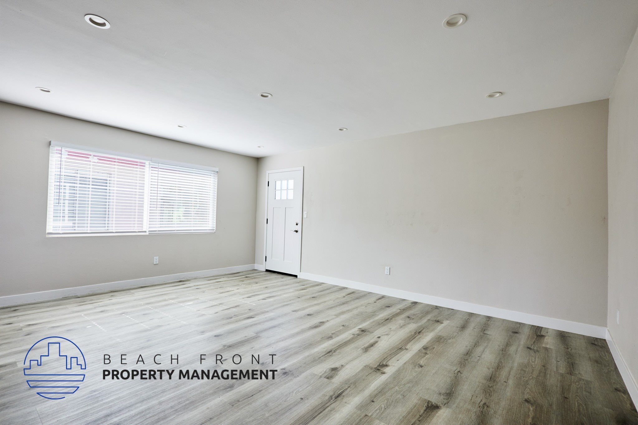 A spacious room with wooden flooring and a window with blinds.